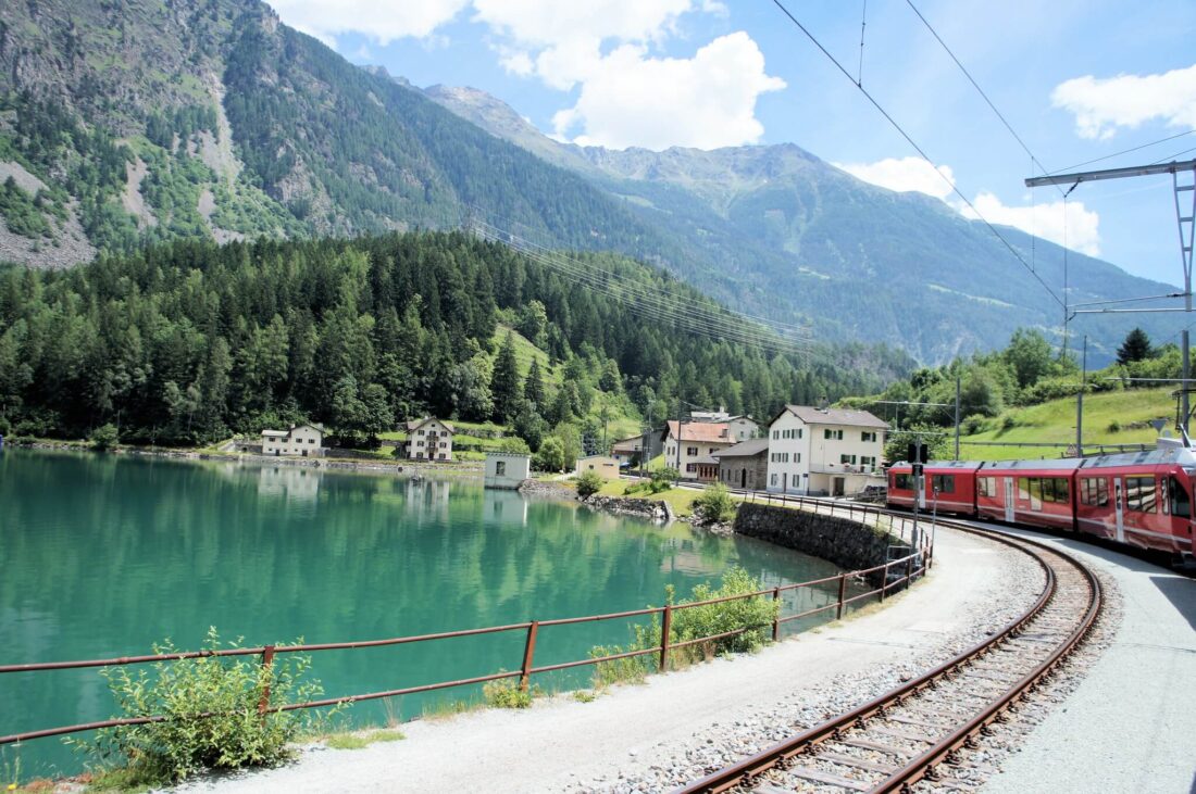 Bernina Express from Switzerland to Italy. A red train riding on the shore of a blue lake.