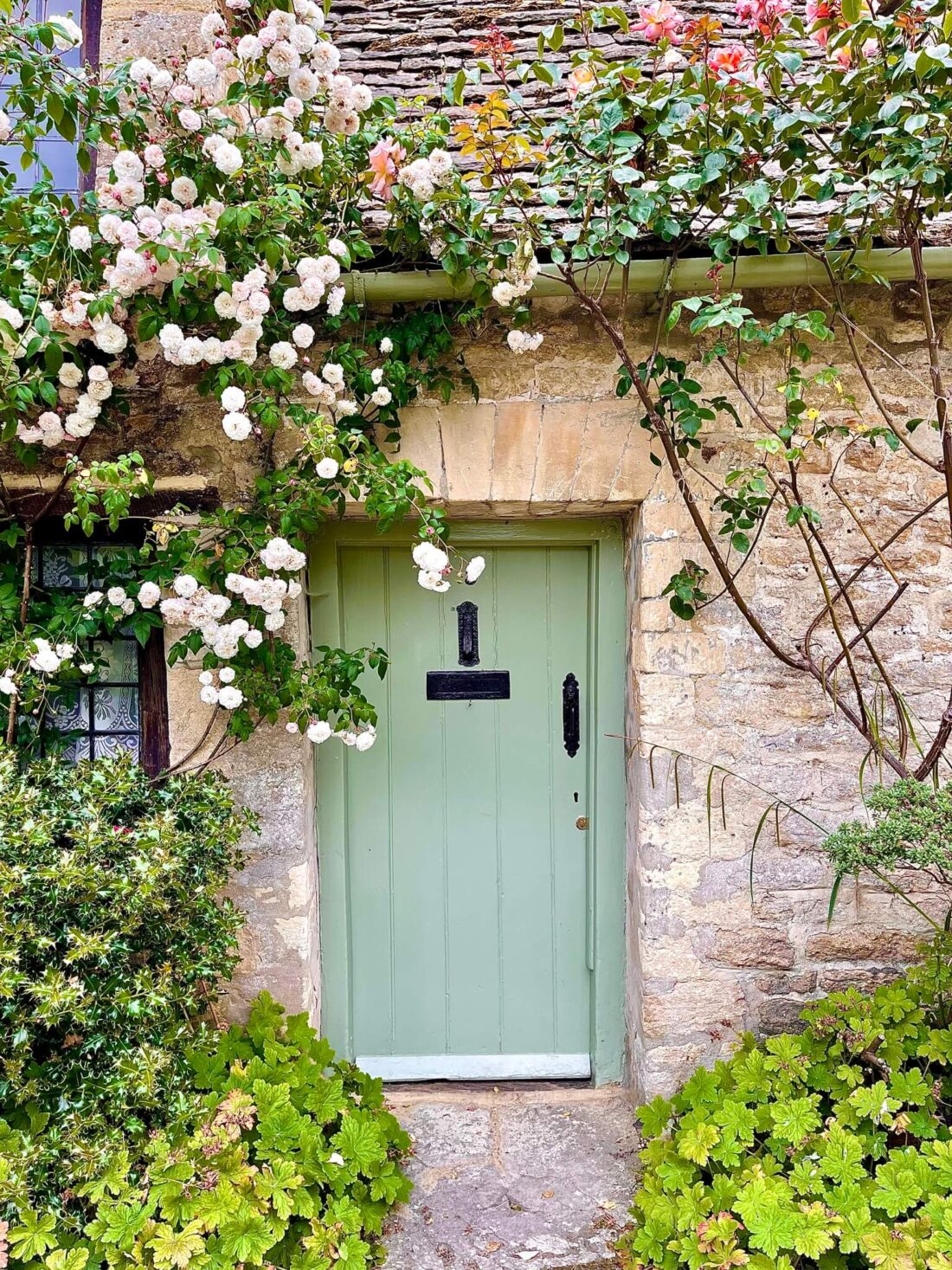 Limestone cottage with green door surrounded by pink roses
Most Beautiful Cotswolds Villages