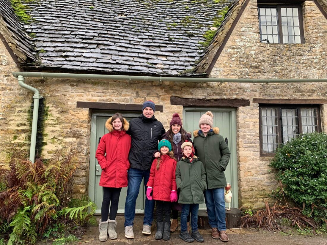 A family standing in front of a limestone cottage in the Cotswolds village of Bibury