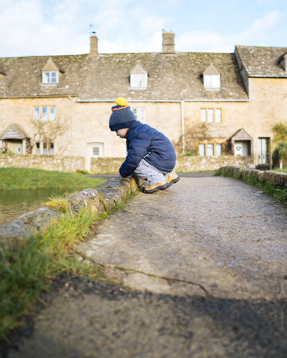 Little boy looking into the river in Lower Slaughter Cotswolds